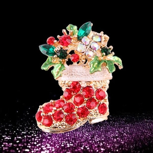 Détail de broche botte de Noël ornée de strass rouges sur un fond noir scintillant
