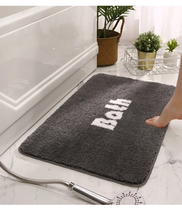 Plush grey rectangular bath mat with white Bath text on white marble floor