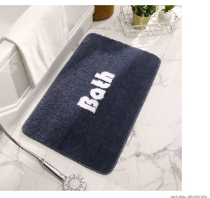 Detail view of a thick navy blue non-slip bath mat with white Bath lettering on marble floor