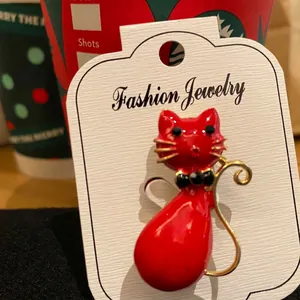 Detail of red enamel cat brooch with gold whiskers and black bow tie on fashion card