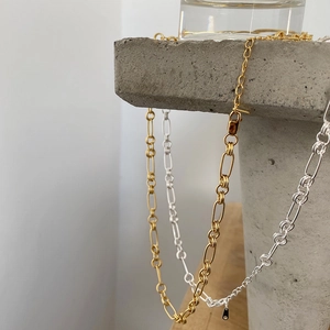 Detailed view of gold and silver minimalist paperclip chain necklaces on stone