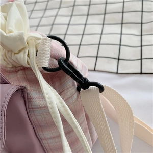 Detail view of pink and purple checkered canvas bucket bag with drawstring and white strap