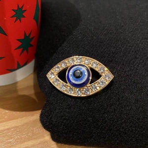 Detail of blue evil eye brooch featuring sparkling white rhinestones on golden alloy