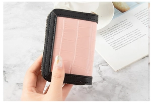 Pink crocodile texture card holder with black zipper detail held over marble surface