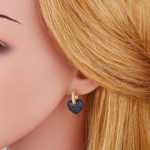 Close-up of heart-shaped blue crystal drop earrings worn on a gold hoop setting