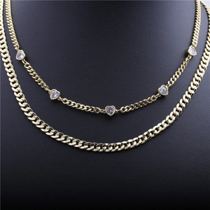 Detail van gelaagde gouden Cubaanse ketting en fijne schakels met zirkonia hartjes