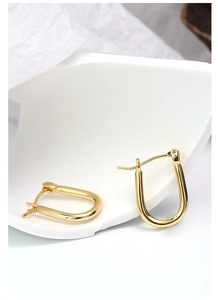 Close-up of gold-plated U-shaped horseshoe earrings on a white minimalist background