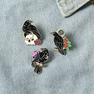 Gothic black raven enamel pin set with skull and rose on denim fabric background