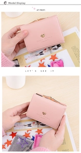 Detail of pink faux leather tri-fold wallet featuring heart-shaped gold buckle and logo
