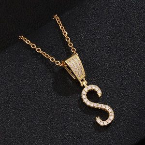Detailed close-up of golden letter S pendant with micro-pave zircons on black leather