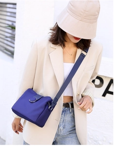 Detail of navy blue nylon crossbody bag featuring wide shoulder strap and circular buckle