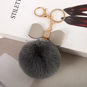 Detailed close-up of dark grey faux fur pom-pom keychain with rhinestone leather bow