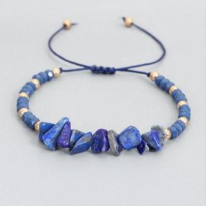Pulsera tejida a mano con piedras azules irregulares y cuentas doradas sobre fondo gris