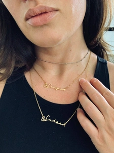 Macro shot of layered gold name necklaces Harper and Hudson on a female model
