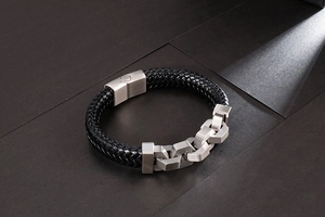 Macro detail of men's black braided leather bracelet with brushed stainless steel clasp