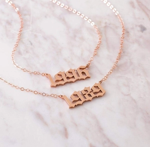 Detail of rose gold custom year necklaces 1996 and 1989 in gothic font on marble background