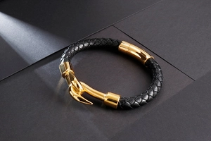 Detailed view of black braided leather bracelet with golden fishhook clasp on stone background