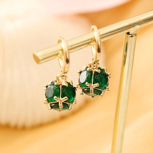 Macro shot of gold earrings featuring emerald green spherical stones with ornate cross inlays