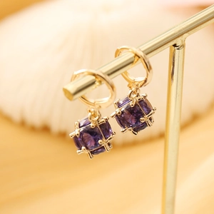Macro shot of gold hoop earrings with purple square crystal in cage setting