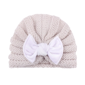 Close-up of baby knit hat showing chunky beige knit texture and large white bow detail