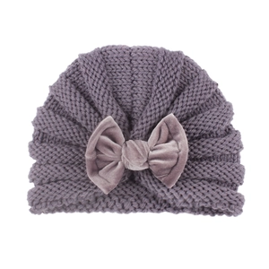 Purple knitted baby hat with a large velvet bow decoration on a white background