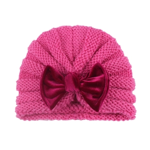 Detail of rose pink baby knit turban hat featuring a large deep red velvet bow decoration