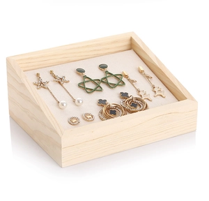 Slanted wooden jewelry tray with beige lining displaying assorted earrings on white background
