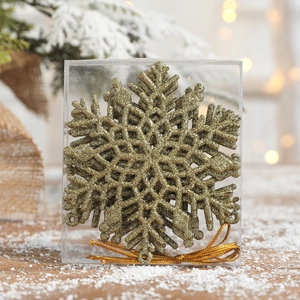 Glittery gold snowflake Christmas tree ornaments in clear gift box with pine branches