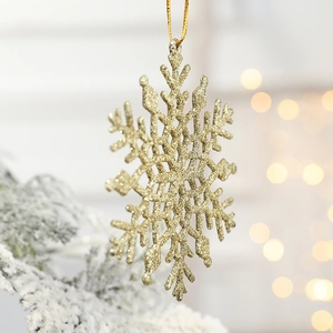 Sparkling gold glitter plastic snowflake ornament hanging on a Christmas tree branch