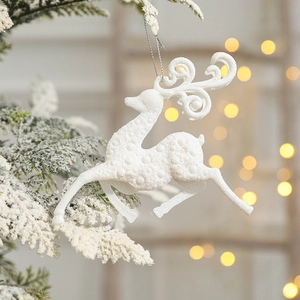 White glittery reindeer hanging ornament on snowy Christmas tree branch with warm lights