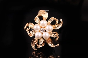 Macro di una spilla a fiore dorato con perle bianche e uno strass lucido al centro