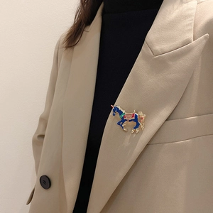 Detail of colorful enamel carousel horse brooch styled on a beige blazer lapel
