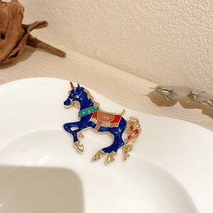 Detailed view of blue enamel horse brooch with gold finish on a white ceramic plate