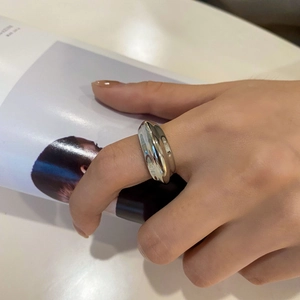 Close-up van een brede zilveren metalen ring met golvend design en gepolijste finish