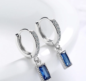 Macro shot of silver drop earrings with emerald-cut blue stones and sparkling zircon details