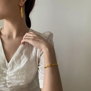 Detail eines 18K vergoldeten Mobius-Armbands und dicker Creolen an einem Model getragen