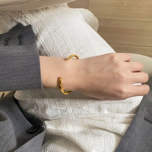 Detail eines goldenen Mobius-Armreifs am Handgelenk über einem eleganten Sakko-Ärmel