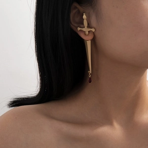 Detail of gold sword earring with deep red teardrop gemstone on female model