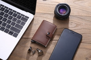 Brown PU leather pop-up wallet with metal frame on a high-end business desktop setup