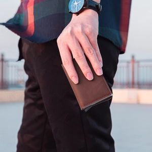 Detail of dark brown leather card holder with automatic pop-up button held by hand