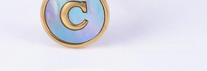 Macro detail of 18K gold letter C pendant with blue shell inlay and relief design