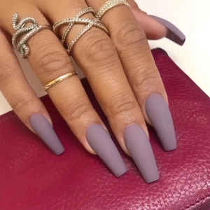 Close-up of matte purple long ballerina press-on nails on a pink textured surface