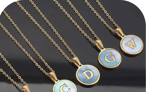 Detail of 18K gold plated initial pendants with blue shell inlay on black surface