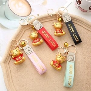 Four golden bull keychains with colorful leather straps and lucky charms on a wooden tray