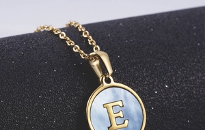 Macro detail of gold 18K stainless steel letter E pendant with blue shell inlay