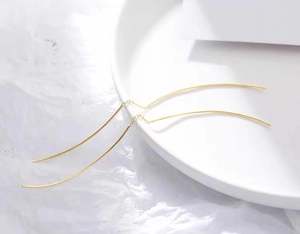 Detail of minimalist long gold-colored tassel earrings on white ceramic background