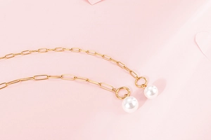 Detail of gold box chain necklace with elegant white pearl pendants on pink floral background