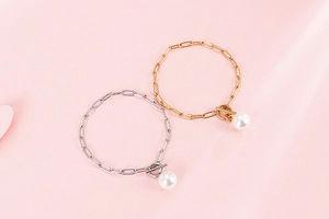 Detail of gold and silver paperclip chain bracelets with T-bar clasp and pearl pendants