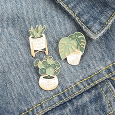 Detail of three enamel pins featuring potted plants on blue denim background