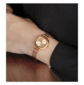 Close-up of a women's gold square watch with a mesh strap on a model's wrist
